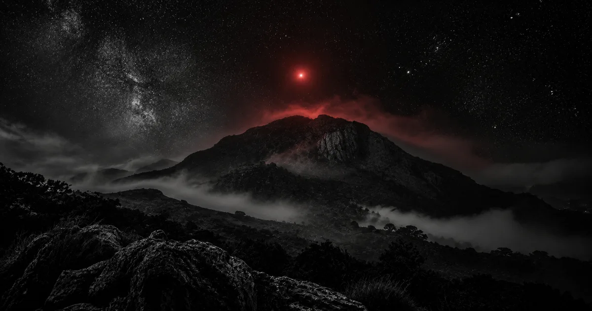 La silueta del Cerro Uritorco recortada contra un cielo nocturno estrellado, con una luz roja anómala suspendida sobre su cumbre entre la niebla