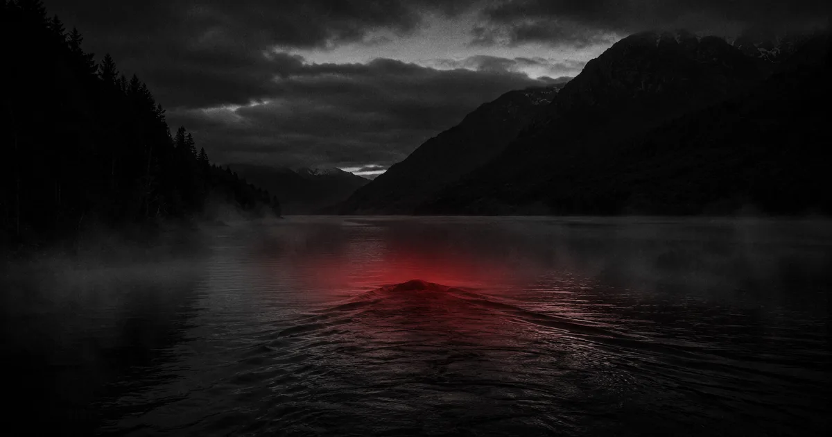 La superficie oscura y quieta del lago Nahuel Huapi al atardecer, con una estela y una silueta ambigua asomando apenas del agua entre las montañas, y un tenue resplandor rojo en el punto donde emerge